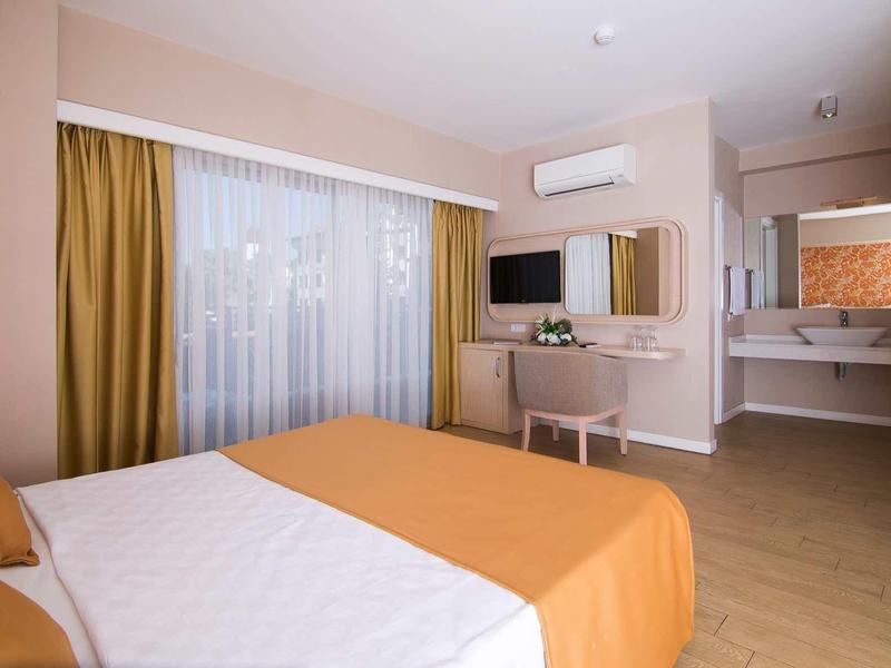 Modern eingerichtetes Schlafzimmer mit großem Bett, gelben Vorhängen, TV und einem Waschbeckenbereich.