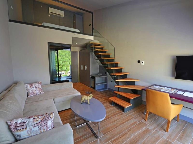 Wohnzimmer mit graßem Ecksofa, Holztreppe, orangem Sessel und Flachbildfernseher an der Wand.