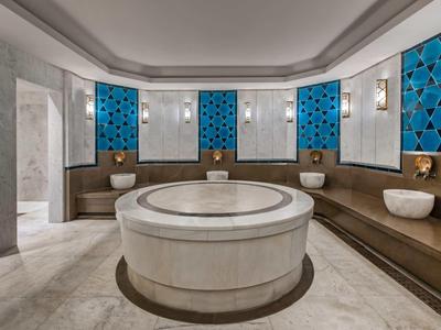 Moderner Hammam mit runden Marmorbrunnen, braunen Sitzbänken und blauen Wandfliesen.