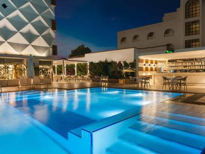 Moderne Hotelbar mit beleuchtetem Pool und Loungemöbeln bei Nacht.