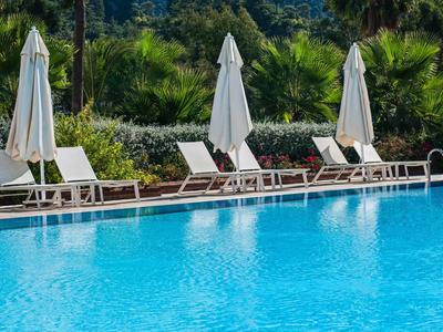 Blauer Swimmingpool mit drei weißen Sonnenschirmen und Liegestühlen, grüne Bepflanzung im Hintergrund.