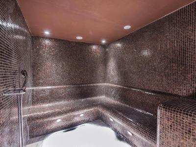 Dunkelbraune Mosaikwand und Sitzfläche in einer eckigen, beleuchteten Sauna.