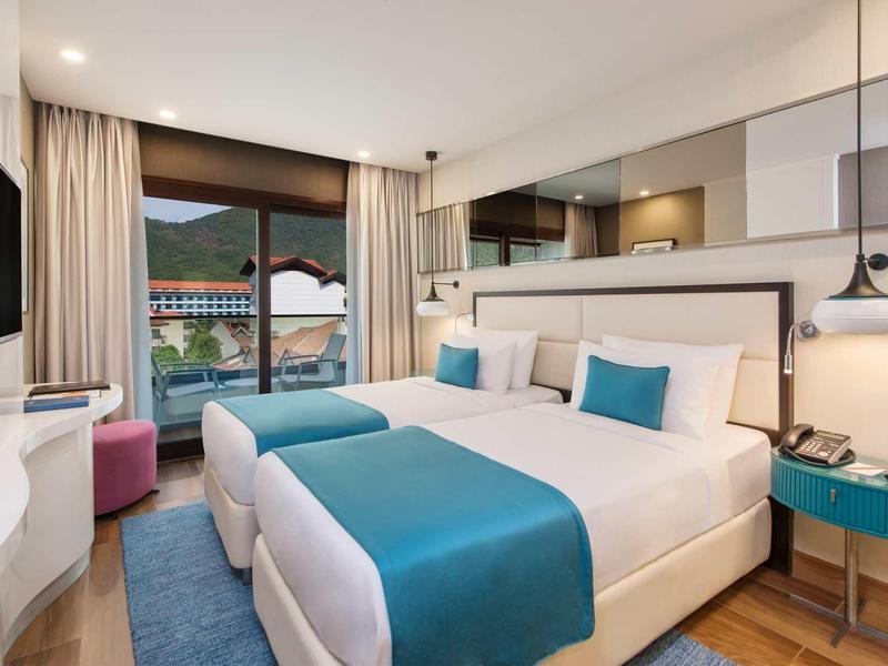 Modernes Hotelzimmer mit zwei Betten, weißen Wänden, blauen Akzenten und Balkon mit Bergblick.