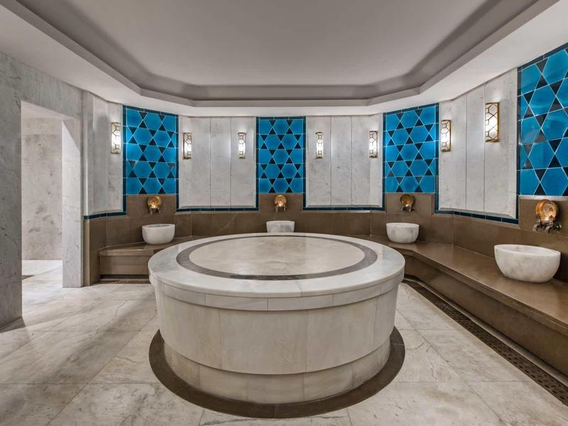 Moderner Hammam mit runden Marmorbrunnen, braunen Sitzbänken und blauen Wandfliesen.