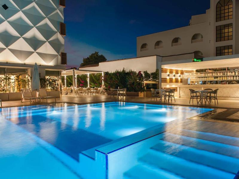 Moderne Hotelbar mit beleuchtetem Pool und Loungemöbeln bei Nacht.