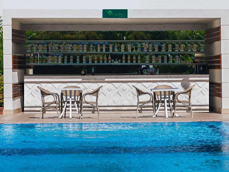 Moderner Poolbar mit weißen Stühlen, Tischen und blauem Schwimmbecken im Vordergrund.