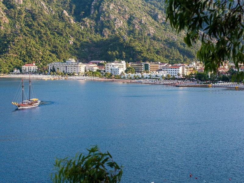Blick auf eine Küstenstadt mit Bergen, blauem Wasser und einem Segelboot auf dem Meer.