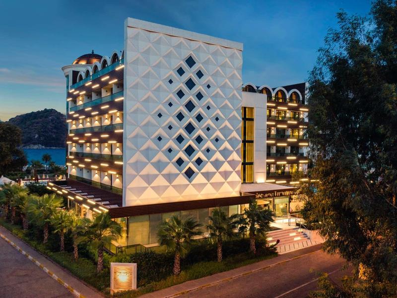 Modernes, beleuchtetes Hotelgebäude mit weißer Fassade und geometrischem Muster bei Abenddämmerung.