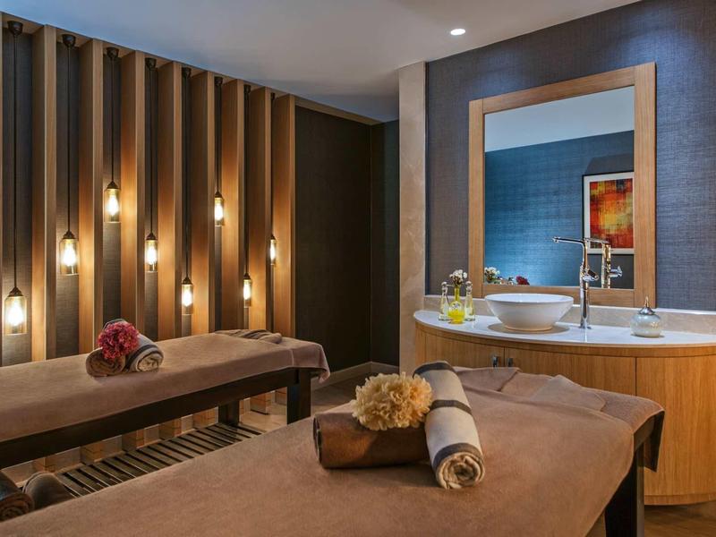 Modernes Spa mit zwei braunen Massageliegen, warmem Licht und dekorativer Wandgestaltung.