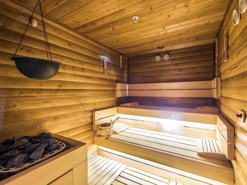 Innenraum einer Holzsauna mit Holzbänken und einem Saunaofen, warme Beleuchtung, helle Holzvertäfelung.