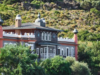 Unikalny budynek z dekoracyjnymi wieżami na tle zalesionego wzgórza.