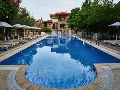 Schwimmbad mit Sonnenliegen und Sonnenschirmen neben einem Hotelgebäude unter Bäumen.