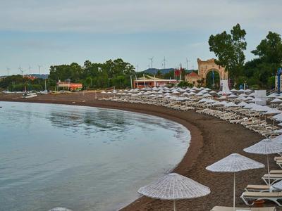 Leerer Strand mit weißen Sonnenschirmen und Liegestühlen am ruhigen Wasser an einer Hotelanlage.