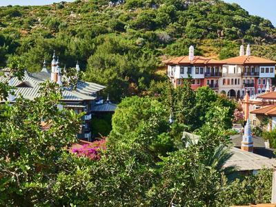 Budynki z czerwonymi dachami otoczone zielonymi drzewami i wzgórzami w tle.