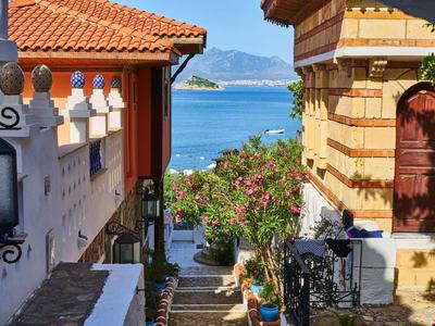 Wąska ścieżka między tradycyjnymi domami z widokiem na morze i góry w tle.