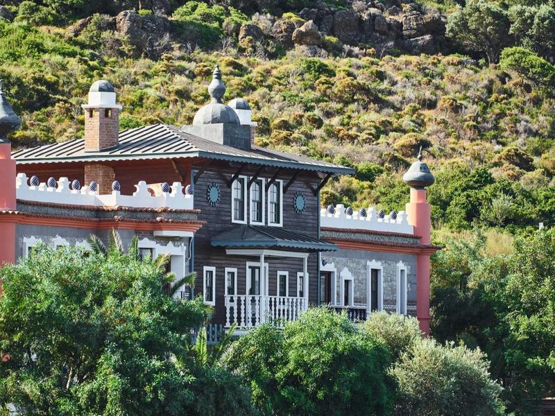 Unikalny budynek z dekoracyjnymi wieżami na tle zalesionego wzgórza.