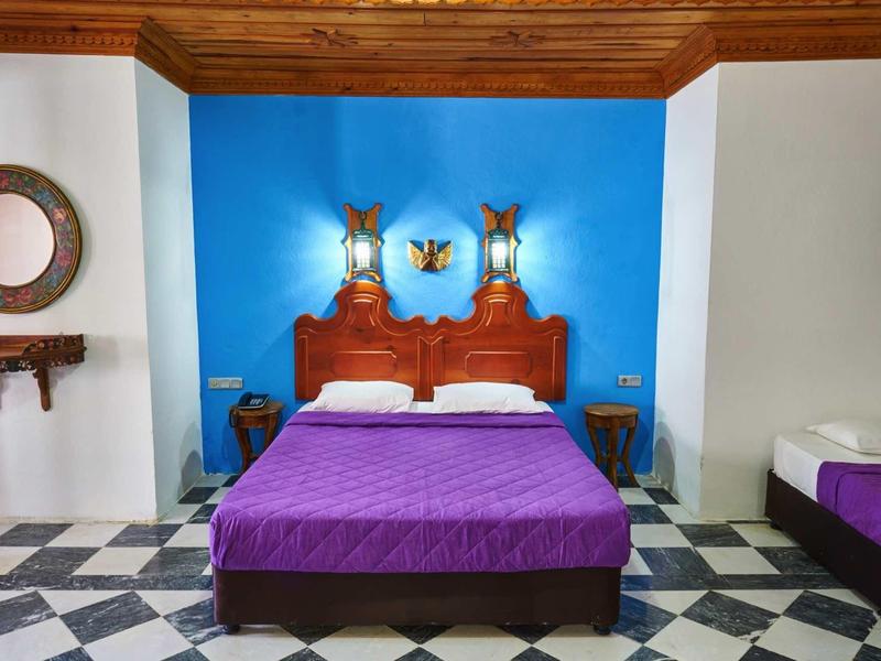 Przytulny pokój hotelowy z niebieską ścianą, drewnianym łóżkiem i kafelkową podłogą.