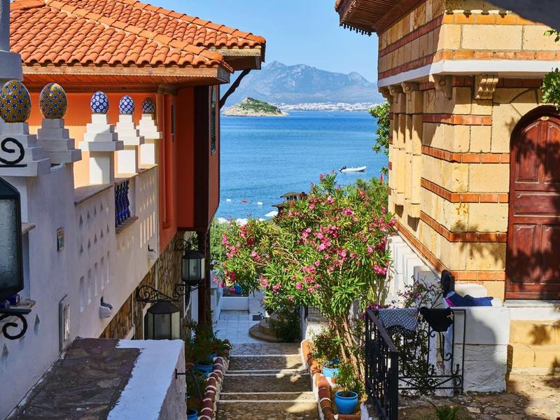 Wąska ścieżka między tradycyjnymi domami z widokiem na morze i góry w tle.