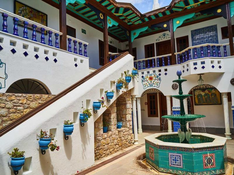 Dziedziniec z schodami, niebieskimi donicami i zieloną fontanną w meksykańskim stylu.