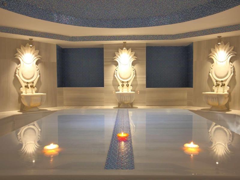 Oświetlone jacuzzi z trzema źródłami wody i pływającymi świecami w spokojnym pokoju.