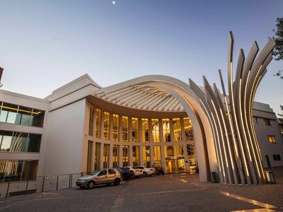 Modern hotel met opvallende gebogen architectuur en verlichte gevel bij zonsondergang.