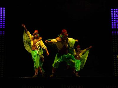 Drie dansers in heldere kostuums treden op een donker podium op.