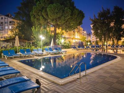 Piscine d'hôtel éclairée avec transats et bâtiments environnants au crépuscule.