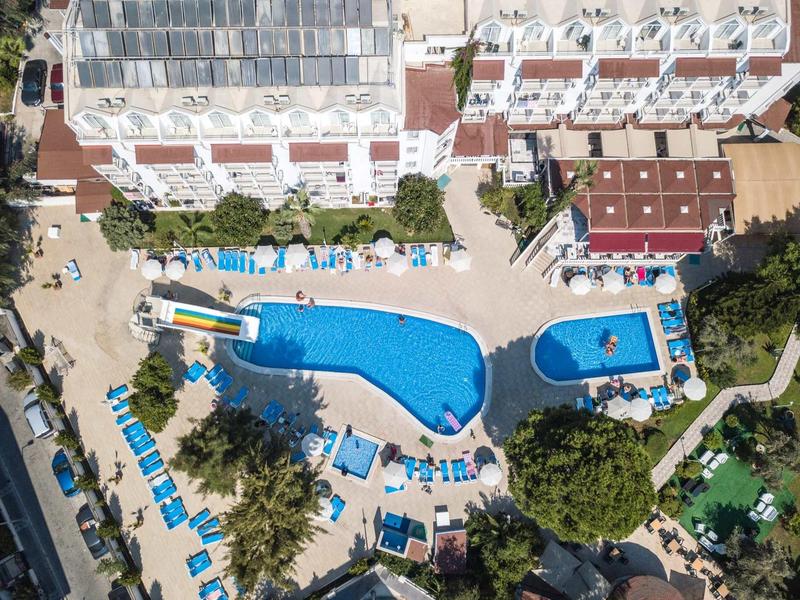 Vue aérienne d'un hôtel avec deux piscines et des chaises longues dans un cadre verdoyant.