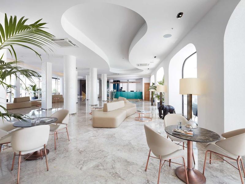 Bright hotel lobby with modern seating, marble floor, large windows, and unique ceiling design.