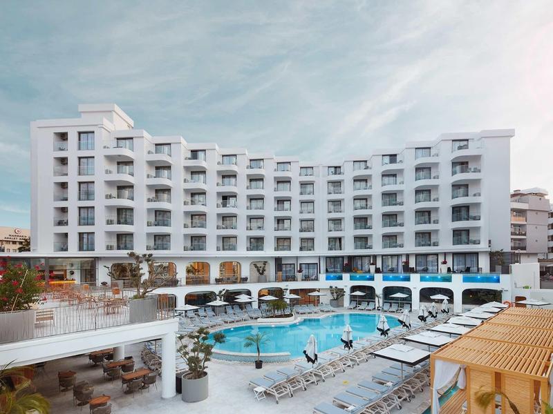 Modern hotel with curved facade, outdoor pool, sun loungers, and cloudy sky.