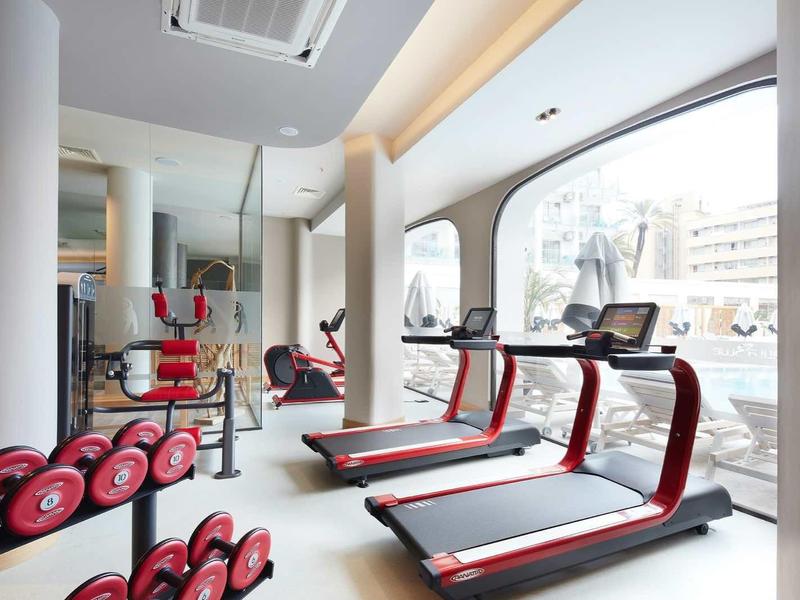 Bright gym with red equipment, treadmills, and large windows overlooking outdoor scenery.