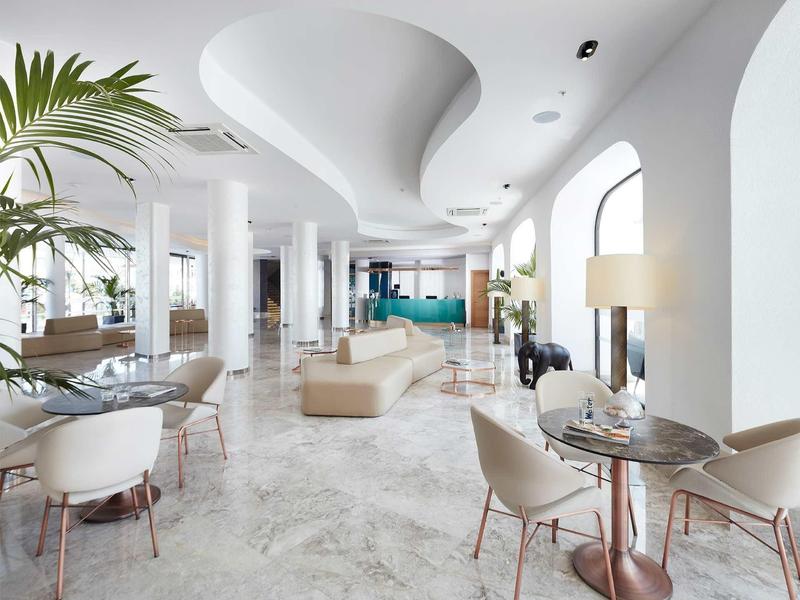 Bright hotel lobby with white columns, modern furniture, and curved ceiling design.