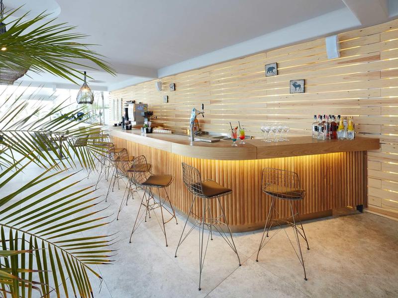 Modern wooden bar with stools and ambient lighting in a bright, open space with decorative plants.