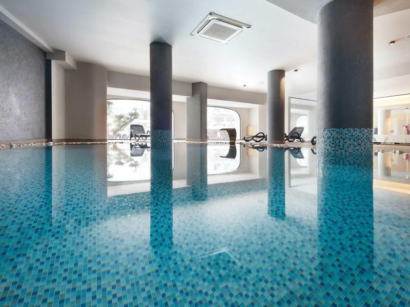 Indoor pool with blue mosaic tiles and large windows letting in natural light.