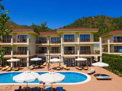 Complexe hôtelier moderne avec piscine, chaises longues et parasols devant une colline boisée.