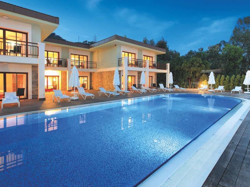 Complexe hôtelier moderne avec grande piscine éclairée et chaises longues au crépuscule.