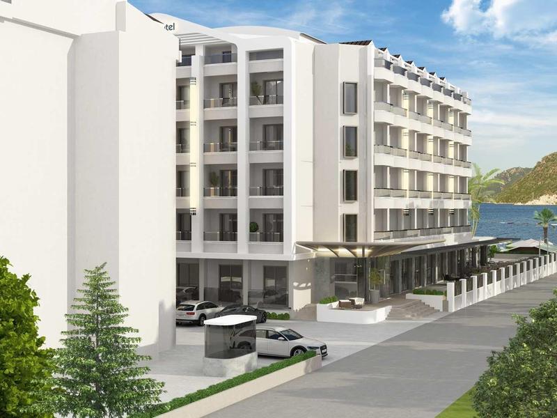 Modernes weißes Hotelgebäude mit mehreren Stockwerken und Terrasse am Wasser unter blauem Himmel.