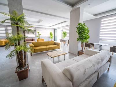 Moderner Loungebereich mit Sofas, Tischen und großen grünen Pflanzen in hellem Raum.