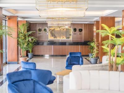 Hotelová lobby s modrým a bílým posezením, elegantní recepcí a rostlinami.