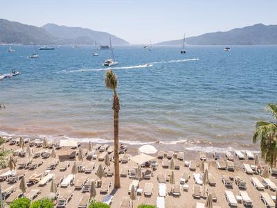 Beach with sun loungers and umbrellas by calm sea and boats under clear sky