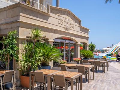 Buitenruimte van een hotel met tafels, stoelen en planten onder een heldere hemel.