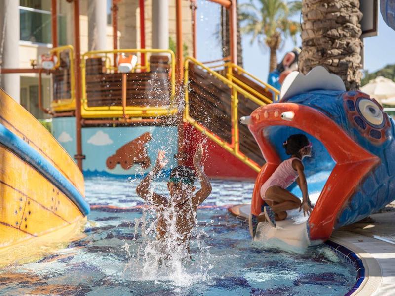 Kinderen spelen en spetteren in het watergedeelte van een hotel speeltuin met kleurrijke glijbanen.