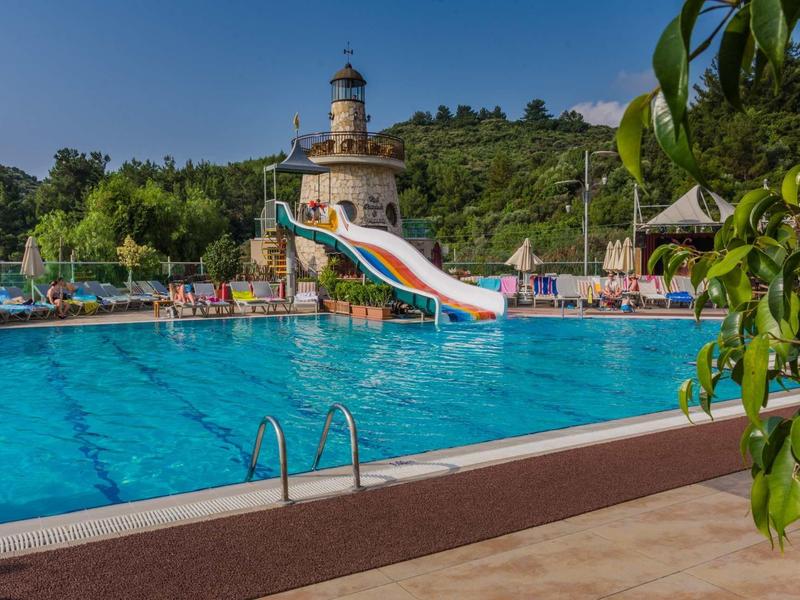 Recreatiegelegenheid met groot buitenzwembad, glijbaan en vuurtoren op de achtergrond bij zonnig weer.