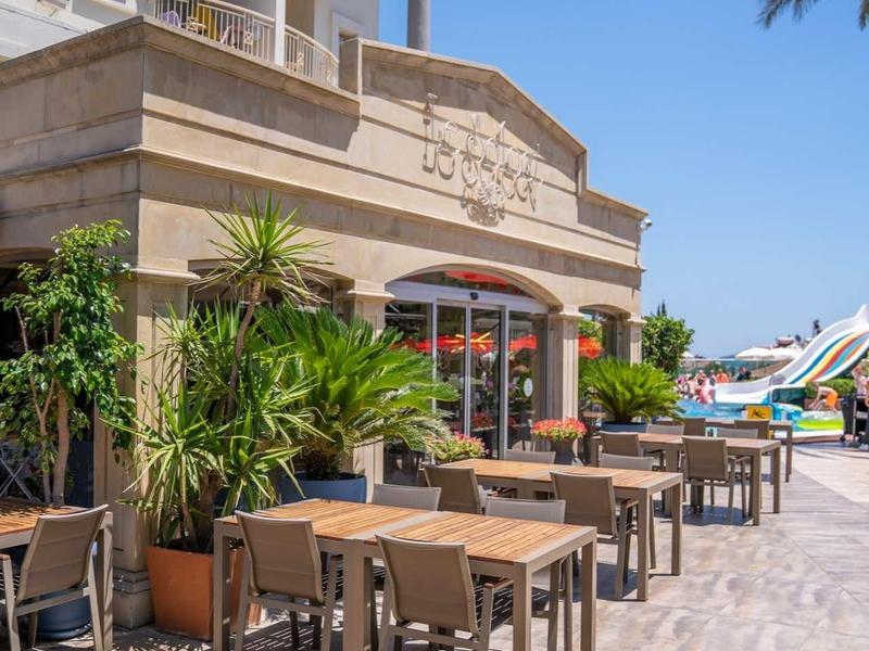 Buitenruimte van een hotel met tafels, stoelen en planten onder een heldere hemel.