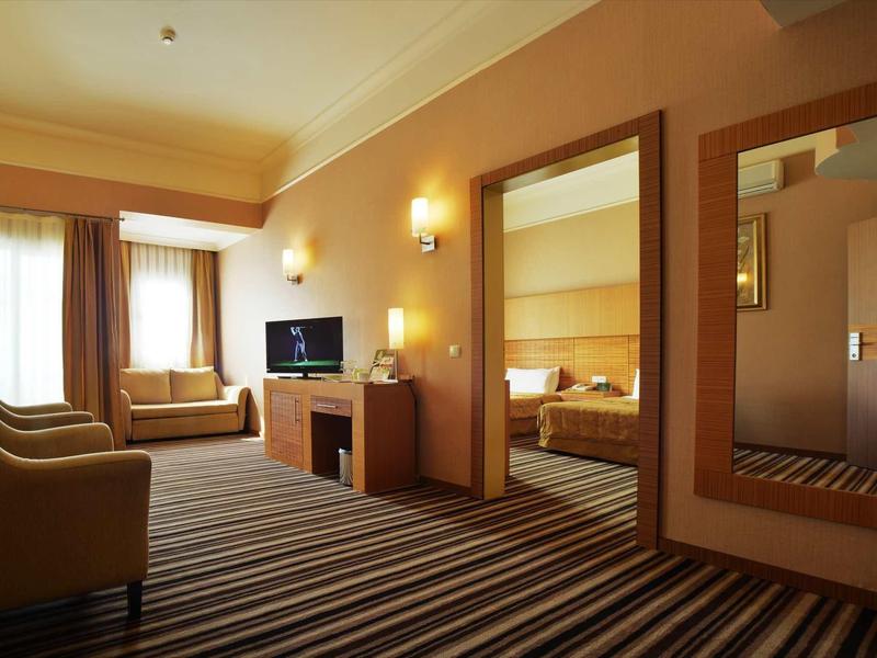 Een hotelkamer met zithoek, tv, bank en aangrenzende slaapruimte.