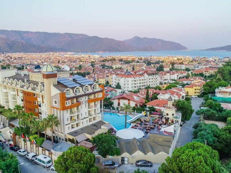 Luxe hotel in een kustplaats met een zwembad, omgeven door groene bomen en bergen op de achtergrond.