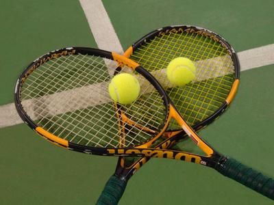Zwei Tennisschläger mit zwei Tennisbällen auf einem Tennisplatz kreuzweise angeordnet.