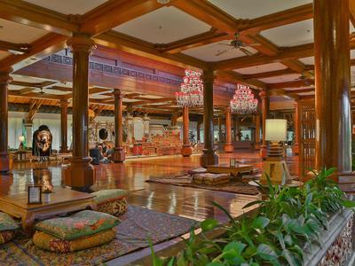 Spacious open hotel lounge with wooden beams, comfortable floor cushions, and abundant green plants.