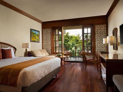 Cozy hotel room with double bed, wooden floor, and a view of the terrace with seating area.
