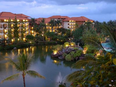 Hotel complex by water with lit buildings and palm trees at dusk.
